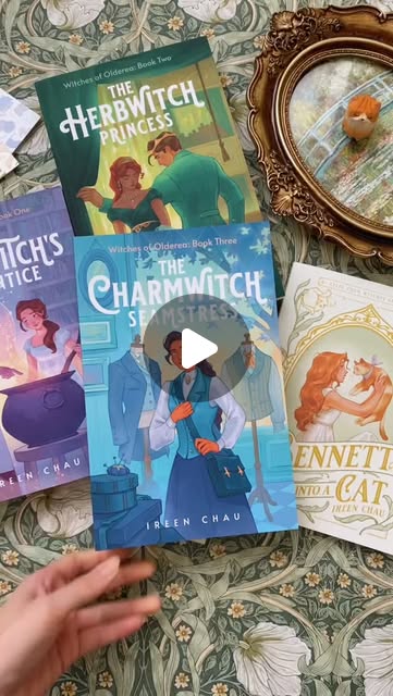 Covers of the Witches of Olderea books by Ireen Chau, including The Herbwitch Princess and The Charmwitch Seamstress, on floral fabric.